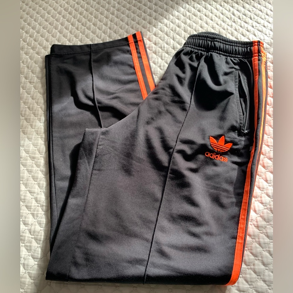 Adidas track pants with orange stripes and logo.